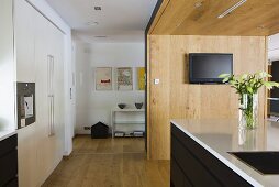 Offene Küche mit Küchenblock vor Holztrennwand und Blick auf Regal im Vorraum