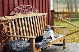 A comfortable terrace with a cat on a fluffy blanket on a wooden bench in front of a red wooden facade