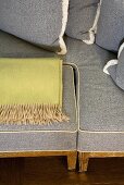 Section of a light gray sofa with a place for stowing a foot stool and a throw