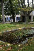 Herbststimmung im Garten mit Seerosenblätter im Teich und altem Landhaus hinter Bäumen