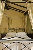 Canopy bed with an elegant black metal frame and white bed linen