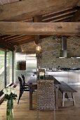 Renovated country home - dining area under a rustic wooden beam ceiling and stainless steel kitchen in front of a natural stone wall