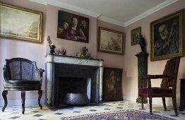 Wohnraum im Altbau mit antiken Stühlen vor Kamin und Bildern vor rosa Wand