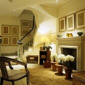 Stimmungsvolles Licht im offenen Wohnraum einer Villa mit Treppenaufgang und weiße Blumen in Töpfen vor dem Kamin