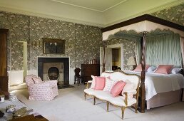 Elegantes Schlafzimmer eines Schlosses mit antiker Sitzbank am Himmelbett mit Baldachin vor Wand mit floralem Tapetenmuster