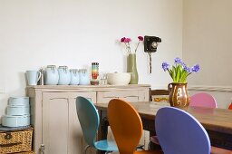 Coloured chairs at a dining table and storage jars on a wooden country-style chest of drawers