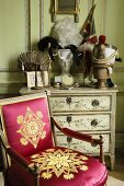 A baroque wooden chair upholstered in shiny red with a gold pattern in front of a painted chest of drawers