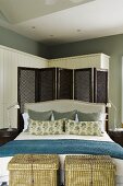 Baskets at the foot of a double bed with a headrest and a dark wooden lattice paravent