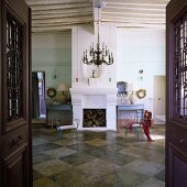Blick durch offene Tür in grossräumigem Wohnraum mit Kamin im Mediterraner Haus und blauen Metallstühlen auf Schachbrettmusterboden