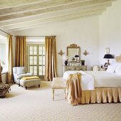 Mediterraner Schlafraum mit Doppelbett und gemütlichem Sessel auf Teppichboden unter rustikaler Holzbalkendecke