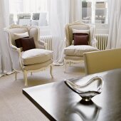 Zwei hellgraue Sessel im Rokokostil vor Fenster mit luftigem bodenlangen Vorhang