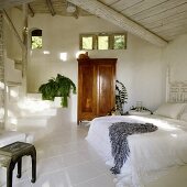 Weisser kühler Schlafraum im tropischen Ferienhaus mit antikem Holzschrank und Treppenaufgang