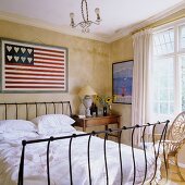 A bed with a metal frame in front of a yellow wall with a stylized American flag