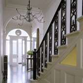 A flight of stairs with black, wrought iron banisters and a chandelier with Medusa arms in front of an archway