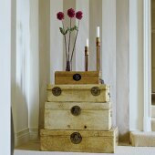 A vase of flowers and a a candlestick on a stack of antique trunks against a striped wall