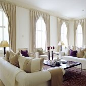weiße Sofagarnitur und Fenster mit bodenlangen Vorhängen im eleganten Wohnraum