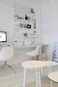 A white corner of a room with a group of stools and a designer chair in front of a workbench below a wall shelf