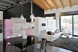 A black table in a designer living room with an open-plan 1950s style kitchen and a wood beam ceiling