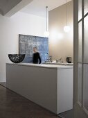 Offene Küche im minimalistischen Vorraum - weiße monolithische Küchentheke und Mann im Flur