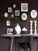 Ceramic vases and candlesticks on a rustic wall table in front of a dark-red wall