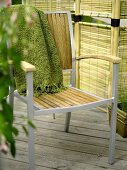 Throw on a garden chair with metal frame and wood seat and backrest in front of a rattan screen