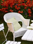 White wicker chair in front of a red flower bed