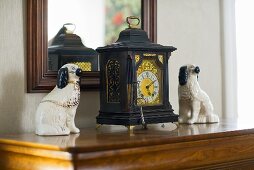 Antique clock and ceramic dog figurines in front of a framed mirror