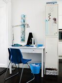 Schreibtisch und blauer Schalenstuhl aus Kunststoff neben weißem Spindschrank