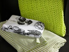 Tablecloths with country house style motifs and striped bed linen next to a green knitted scarf