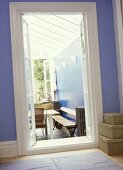 A detail of a blue hallway, looking through an open door to a modern, country conservatory beyond