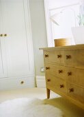 A detail of a modern bedroom with a wood chest of drawers, fitted wardrobe, furry rug