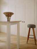 A detail of a modern, country kitchen with dining area, painted units, table, wood stool with leather seat, wood floor, dried seed arrangement