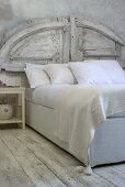 A bed with a rustic, white-painted headboard and white bed clothes