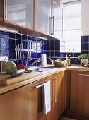 A detail of a modern kitchen, wood units, sink, blue tiling, glass fronted cupboards,