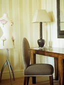 Schneiderpuppe neben grauem Polstersessel und Wandtisch mit Tischlampe