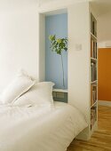 A view of a modern bedroom with blue painted recess, double bed, wooden floor, shelving,