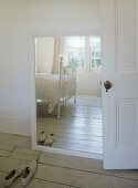 White room with Victorian frame bed reflected in mirror, pair of shoes and wooden floor.sense of space,