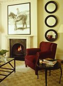 A traditional, sitting room with fireplace open fire, velvet upholstered chair, pattern floor, side table,