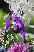 A purple Christmas bauble with a bow hanging from a candle stick