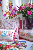 Teepause auf Bett mit bunten Kissen und Blumenstrauss