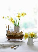 A cake in a shallow glass bowl and daffodils in various vases