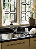 Arbeitsplatte aus schwarzem Granit mit Edelstahlspüle und Zimmerpflanze vor Bleiglasfenster