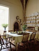 Esszimmer in einem Landhaus mit antiken Kiefernholz-Stühlen, einem quadratischen Tisch mit cremefarbener Tischdecke und antikem Küchenbuffet mit Tellerregal