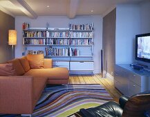Offener Wohnraum mit orangefarbenem Sofa übereck vor Bücherregal und Teppich mit geschwungenen Streifen