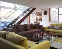 Verschiedenfarbige Sofagarnituren vor Glastisch und freitragende Treppe im offenen Wohnraum