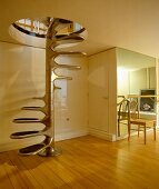 Edelstahl-Wendeltreppe mit freitragenden, ovalen Stufen vor cremefarben glänzender Einbauwand in offenem Raum mit Dielenboden