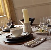 Festlich gedeckter Esstisch mit Kerze in Keramikhalter und Geschirr in Weiß und Braun auf Bast-Sets