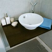 Runde Waschschüssel mit Designer-Armatur auf Waschtisch in dunklem Holz vor hellgrauen Mosaikfliesen