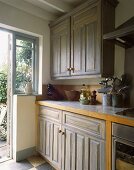 Blaugraue Einbauküche im Landhausstil mit beige-blauem Fliesenboden und offener Tür zum Garten