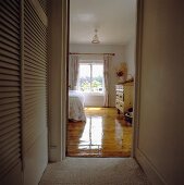 Blick von Schrankraum durch offene Tür auf spiegelnden lackierten Dielenboden in Landhaus-Schlafzimmer